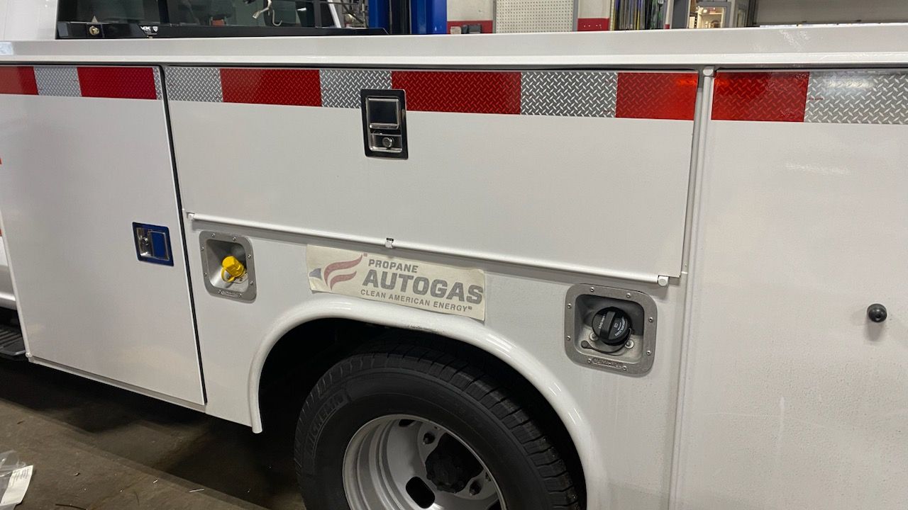 White utility truck with red reflective striping and side storage compartments, parked indoors