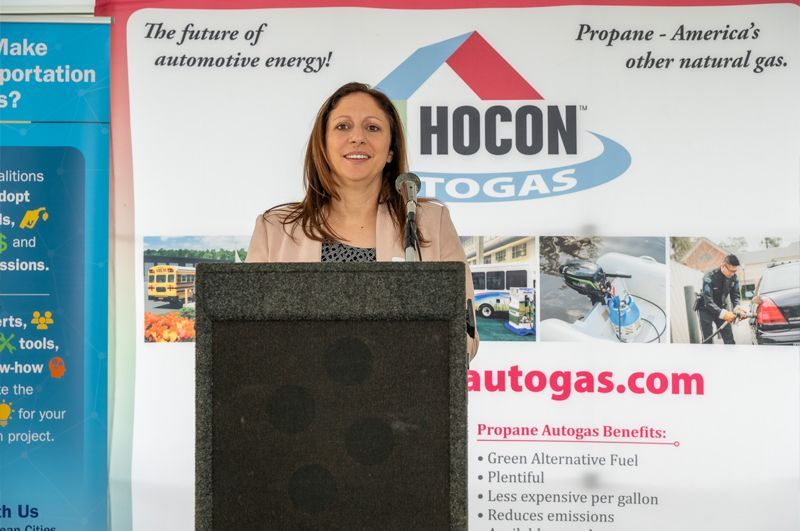 Woman speaking at a podium during a Hocon Gas presentation, with company banners behind her.