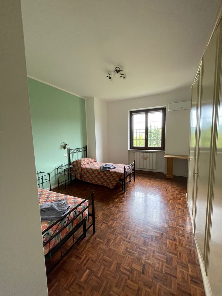 Due letti in una stanza con finestra, parete verde e pavimento in legno.