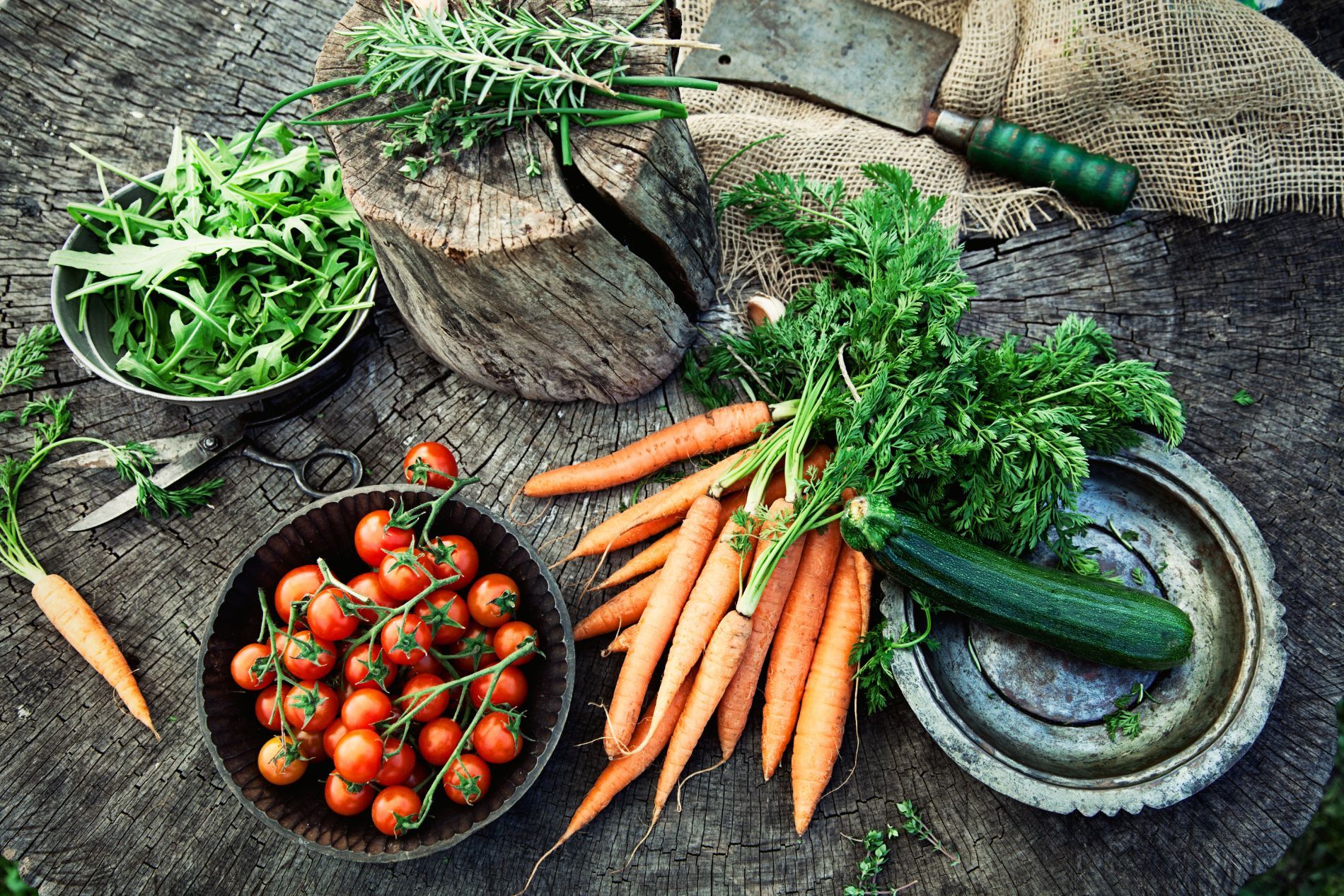 Verdure fresche su una superficie rustica in legno: carote, pomodori, zucchine, verdure a foglia.
