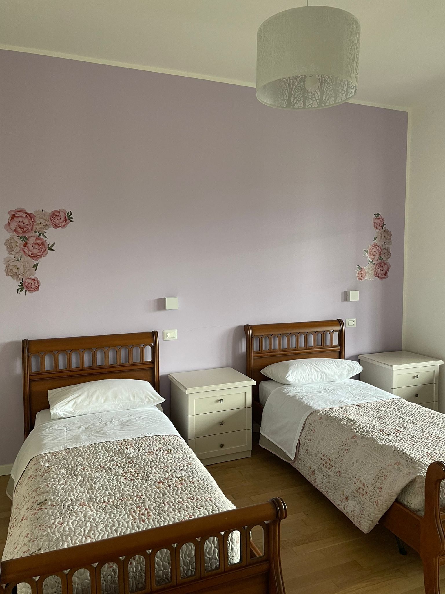 Due letti in una stanza con pareti color lavanda, decalcomanie floreali e paralume decorato.