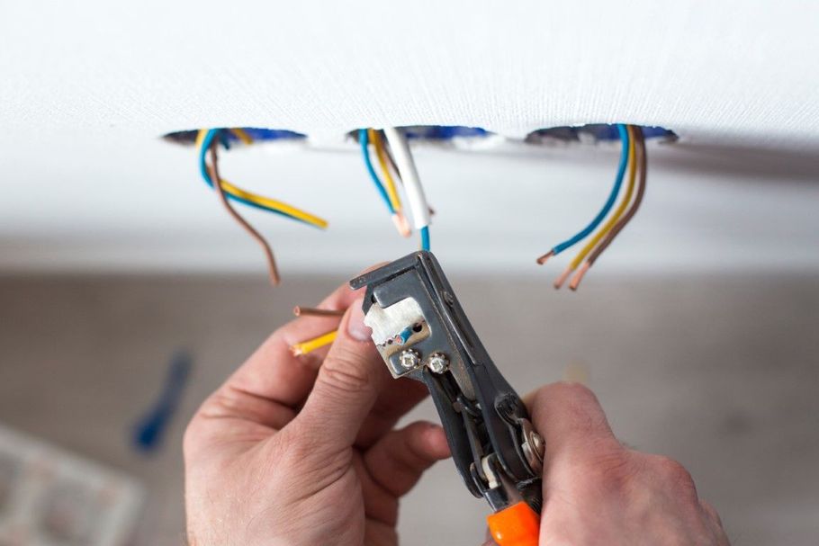 Hands stripping electrical wires from a wall junction box with a tool