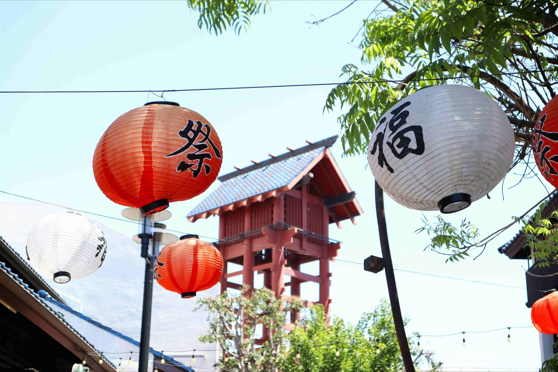 Japanese paper lanterns hanging in Little Tokyo, Los Angeles, with a traditional-style tower and greenery in the background.