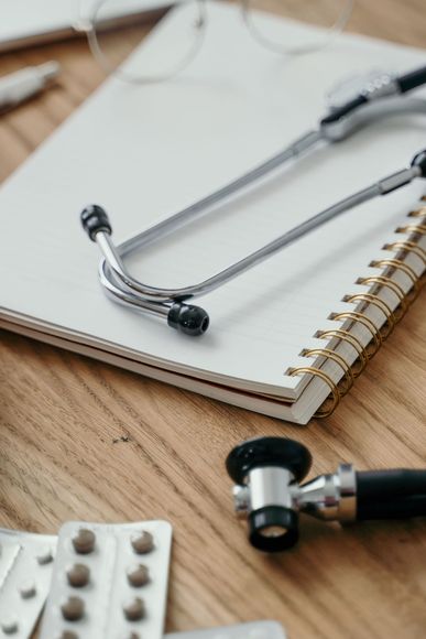 Stethoscope on a notebook beside a blood pressure cuff and pills on a wooden desk