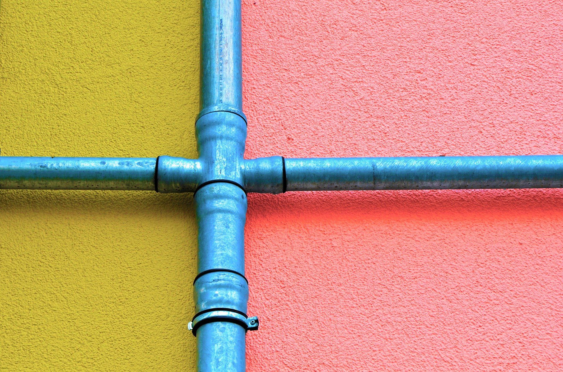 Galvanized metal pipes form a cross on yellow and peach textured wall.