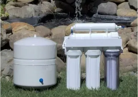 Water filtration system with tank and filters on grass, with a rock and water background.