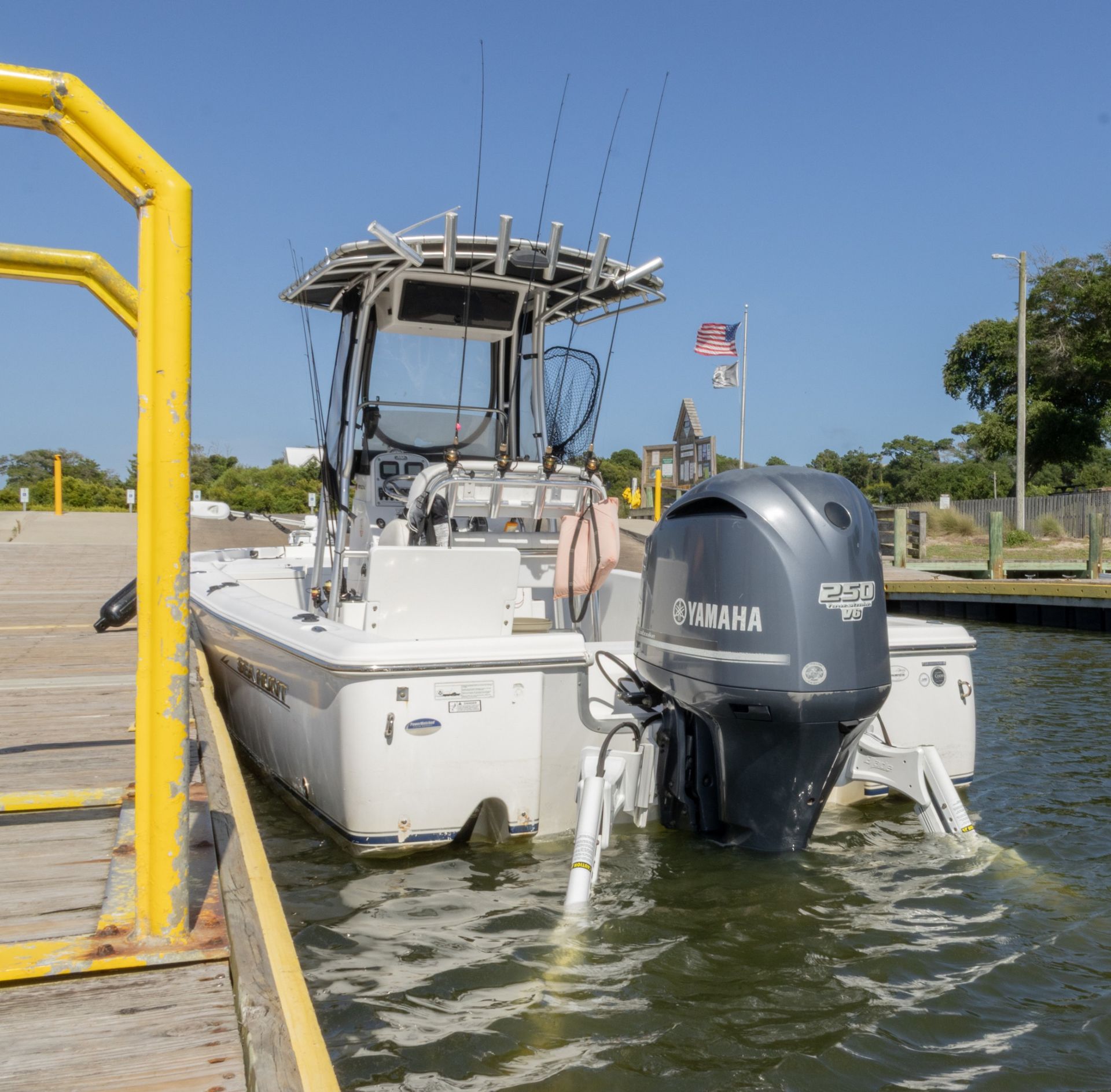 White fishing boat with gray Yamaha motors docked beside a yellow dock in calm water under a clear sky