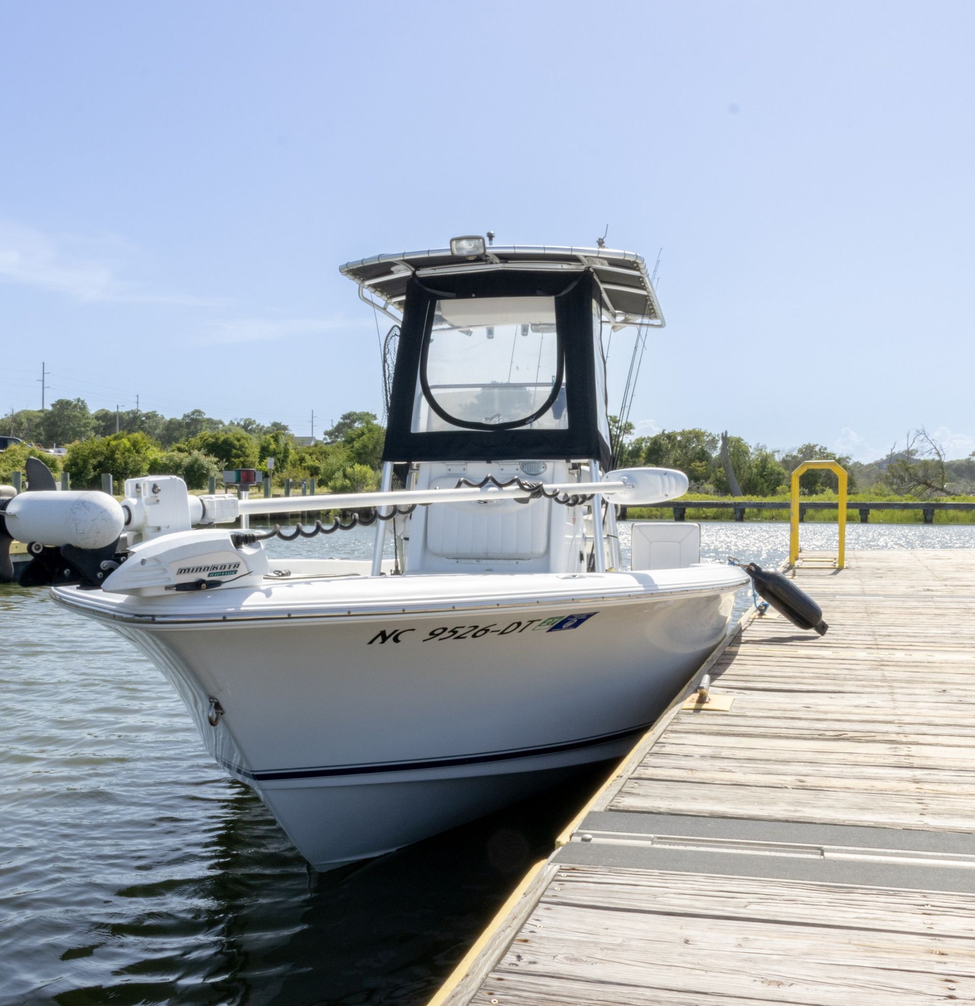 White motorboat docked at a wooden pier on calm water under a clear blue sky