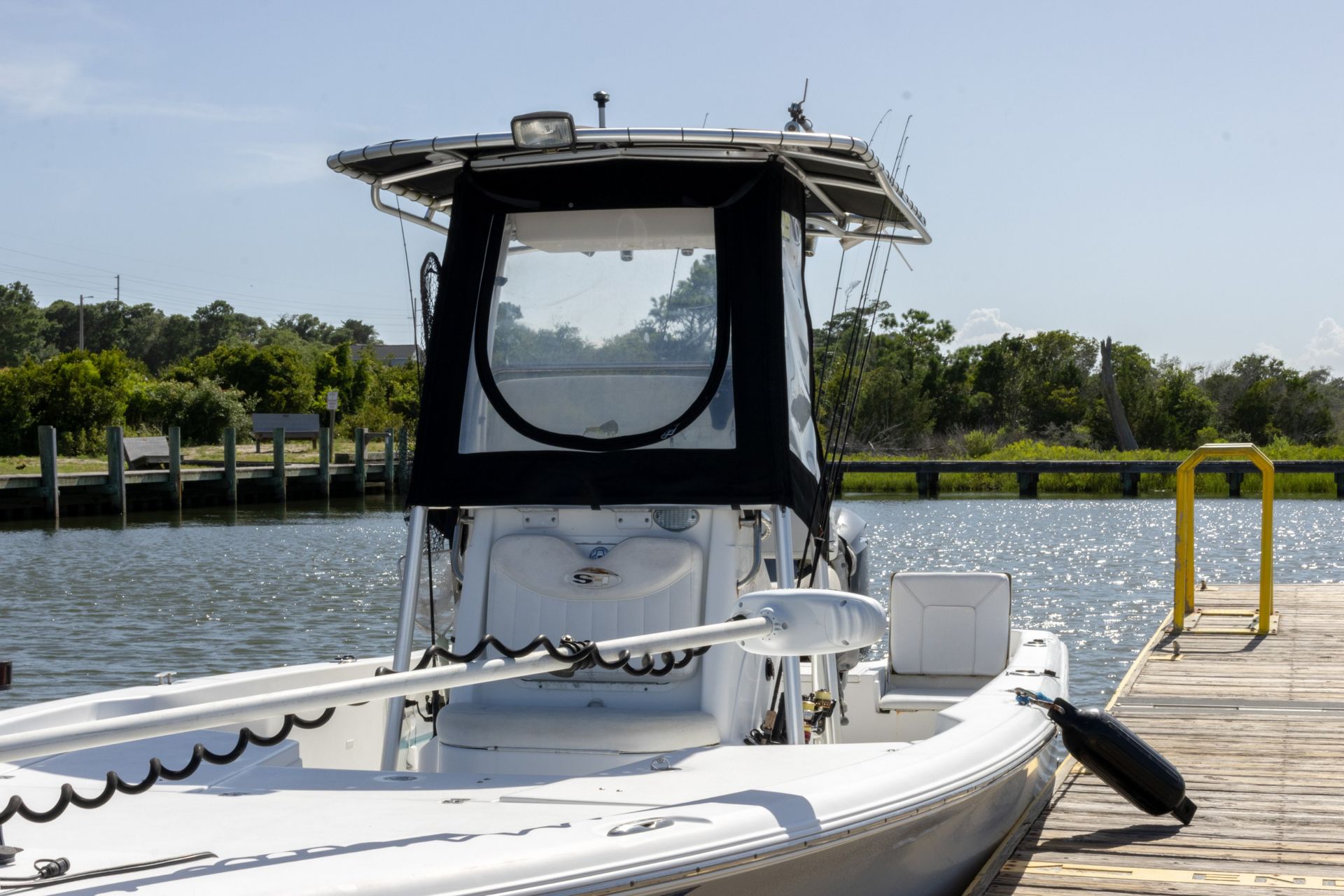 White boat docked at a marina, with a canopy and calm water in the background