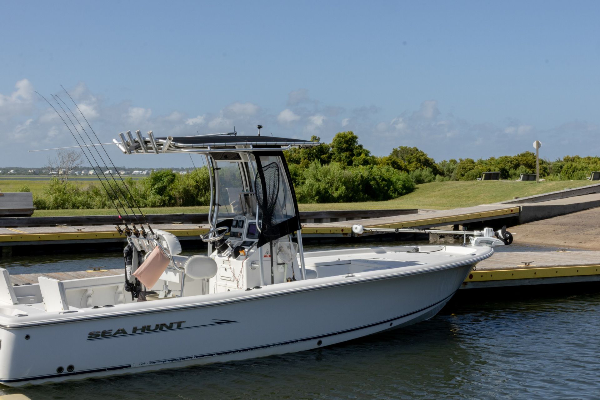 White motorboat docked by a canal beside a grassy shoreline under a blue sky