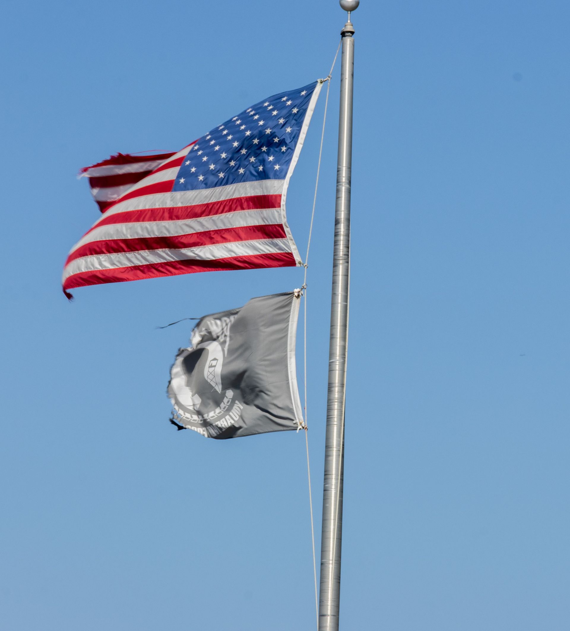American flag flying above a black POW/MIA flag on a pole against blue sky