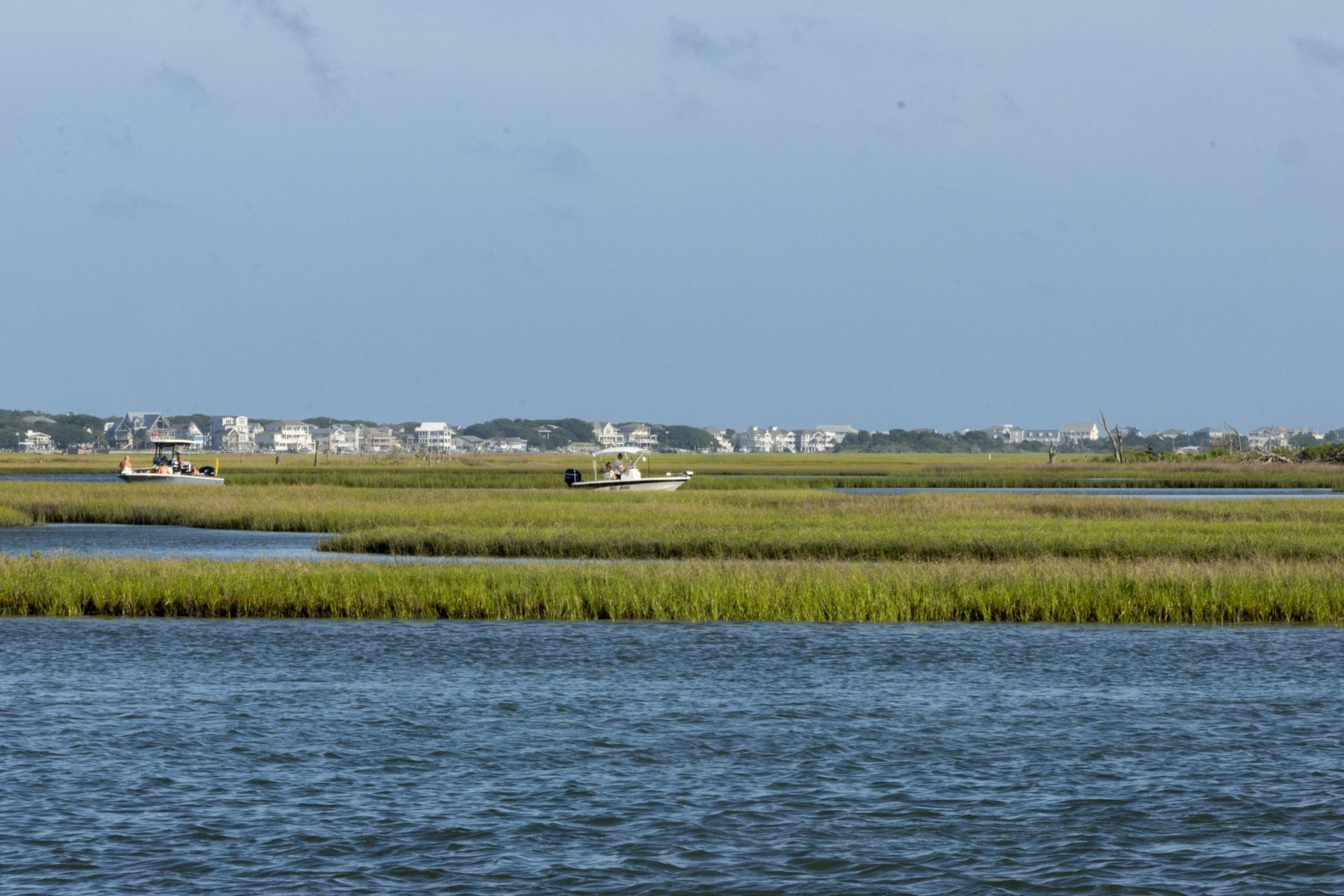 Small plane over marshland and water with houses in the distant background