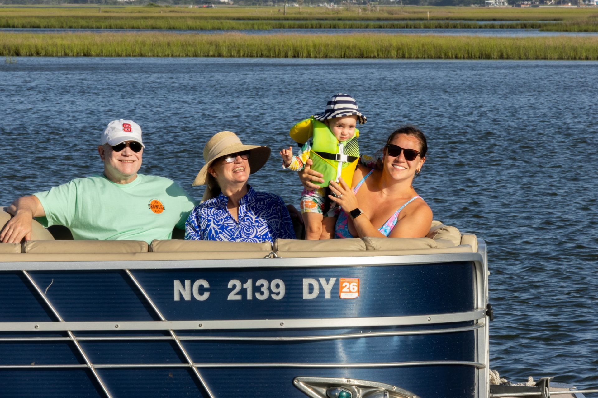 Four people on a pontoon boat on calm water, smiling under a blue sky