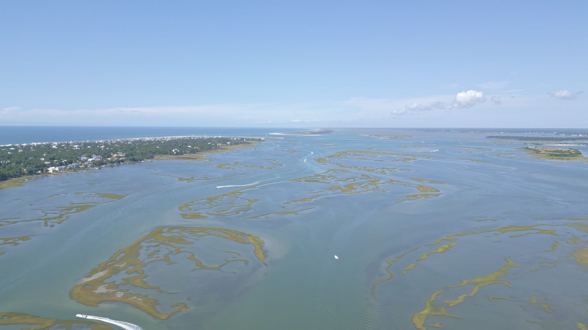 Aerial view of a wide blue lagoon with mangrove islands and a distant shoreline under a clear sky