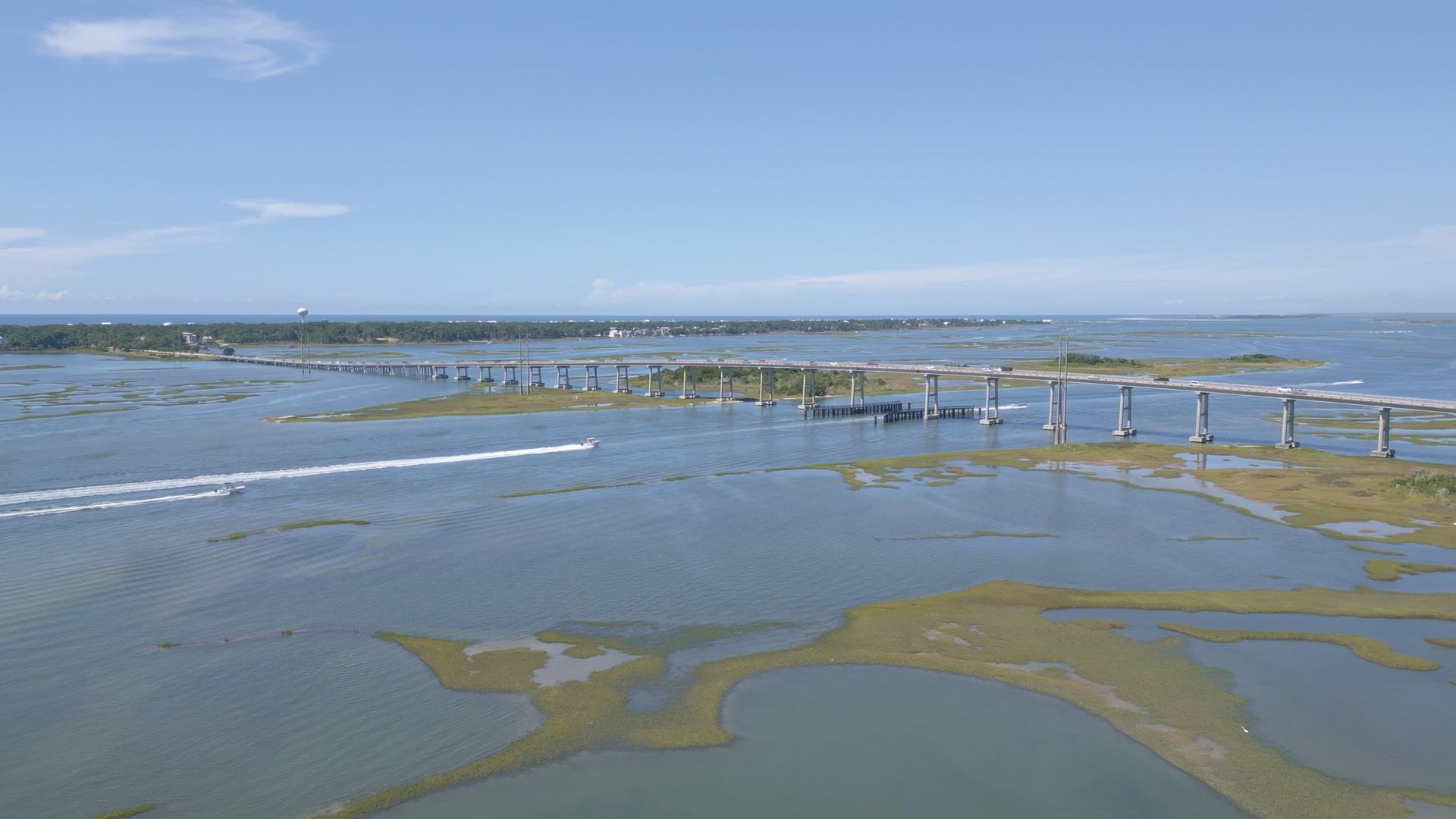 Shallow coastal marsh with wooden boardwalk railing under a blue sky
