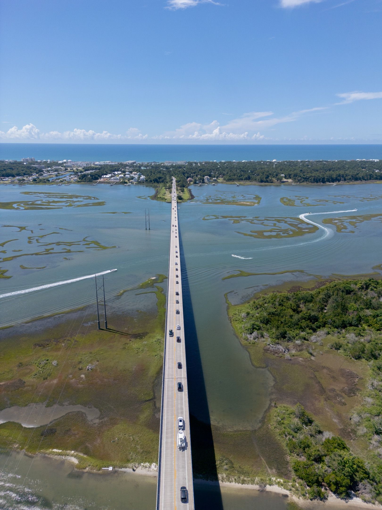 Long bridge stretching over shallow blue water toward a distant coastal town under a clear sky