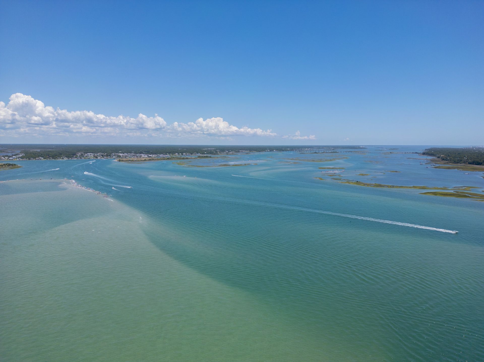 Aerial view of a blue-green bay with distant shoreline and clouds under a clear sky
