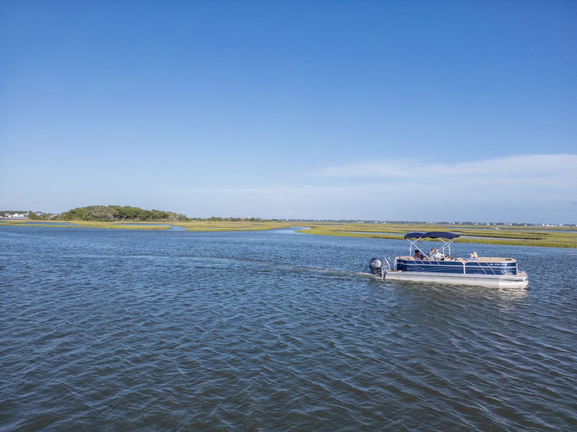 Small motorboat on rippling blue water near a grassy shoreline under a clear sky