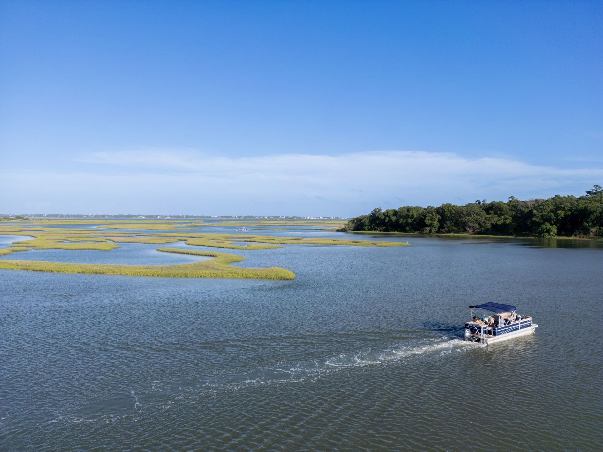 Small motorboat cruising across a calm blue marsh with green islands under a clear sky.