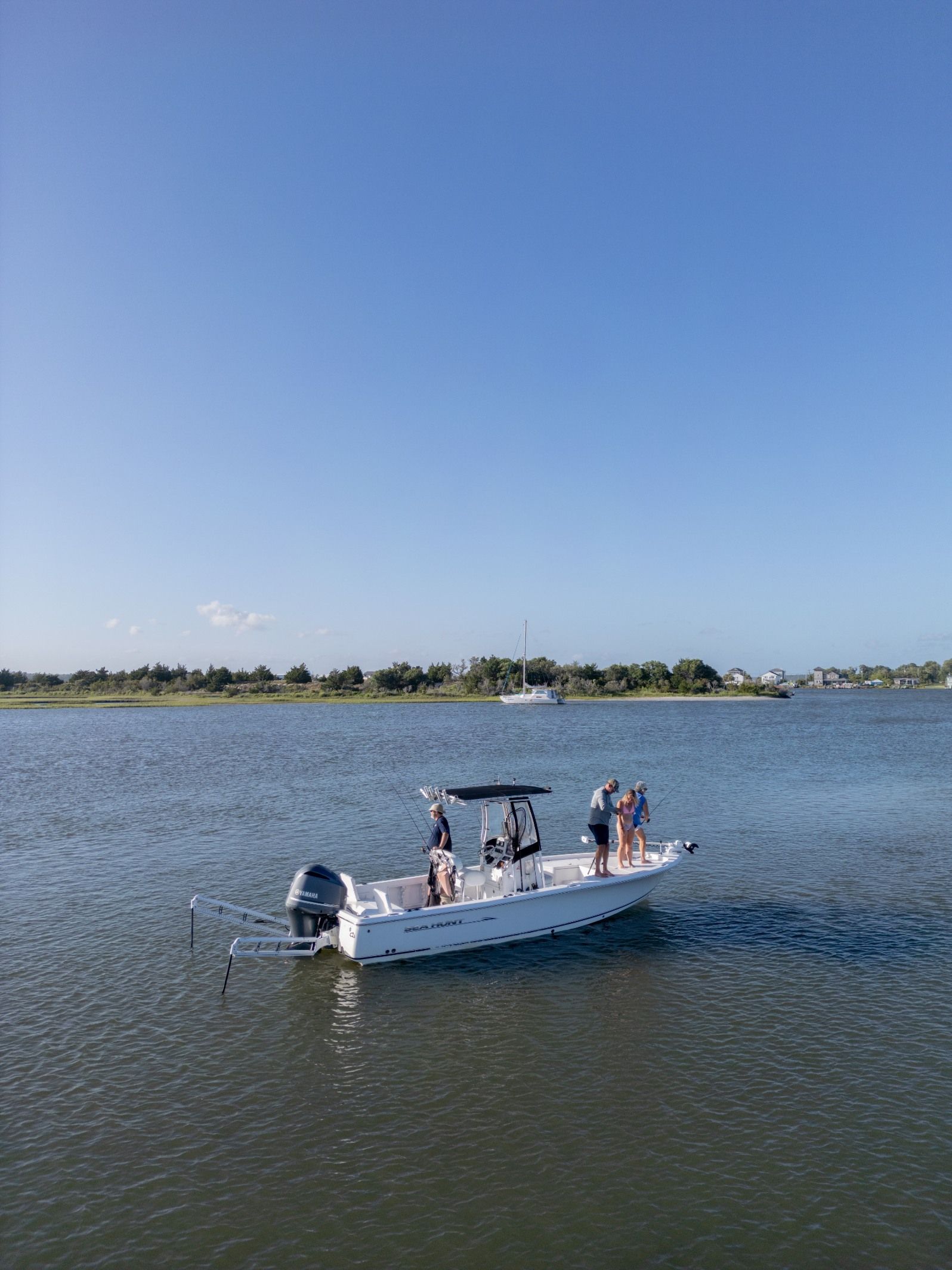 Small white boat with several people on calm water under a clear blue sky near a distant shoreline