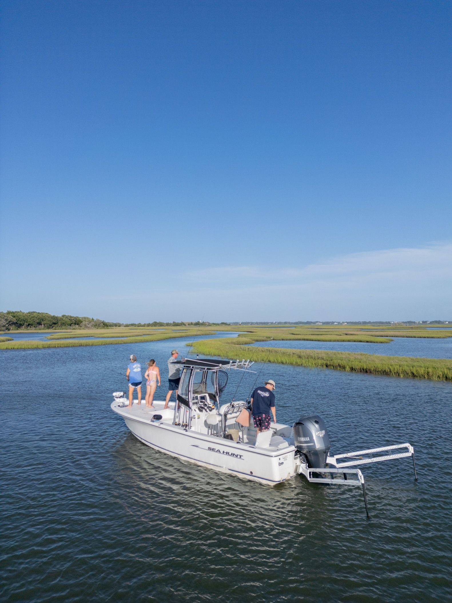 White pontoon boat with people cruising on a calm blue marsh lake under a clear sky