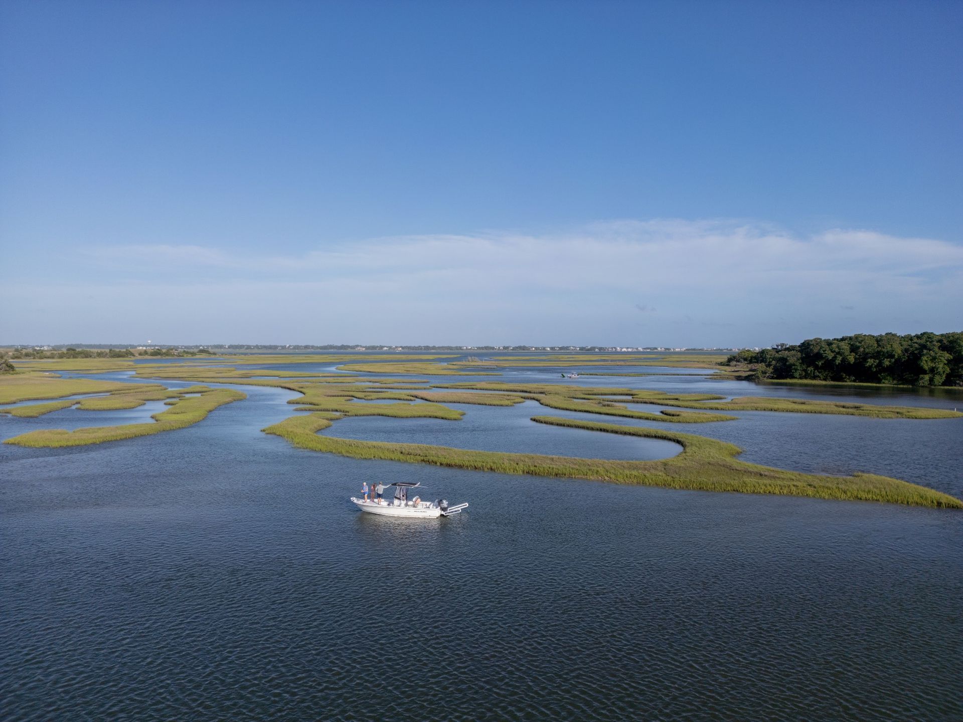 Wide blue marshland with winding water channels and a small white boat under a clear sky