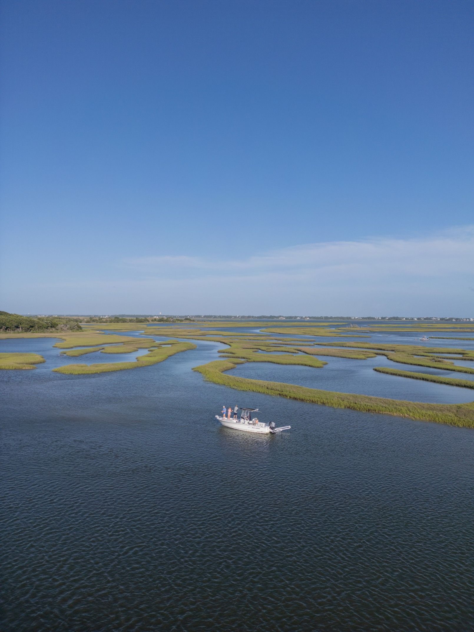 Small white boat on blue water amid green marsh islands under a clear sky
