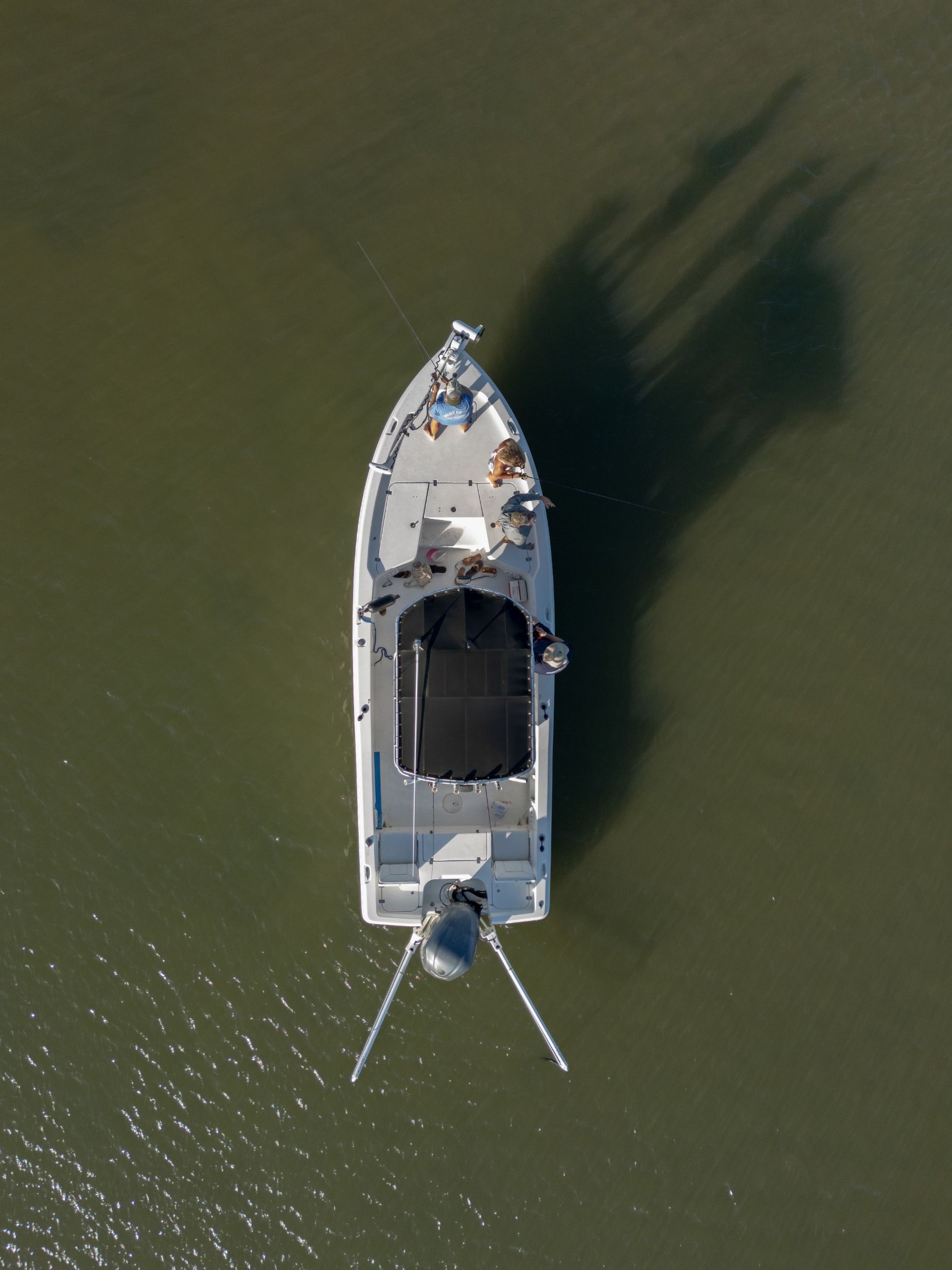 Overhead view of a small boat on green water, with its shadow cast to the right.