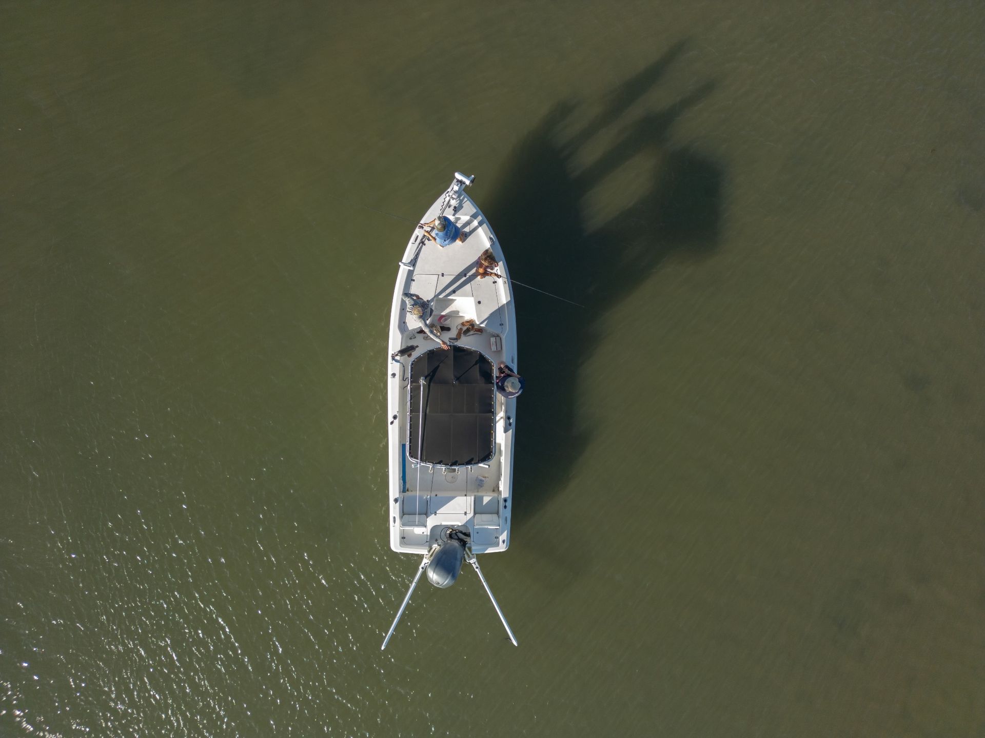 A small white boat seen from above floating on green water, with its shadow cast beside it.