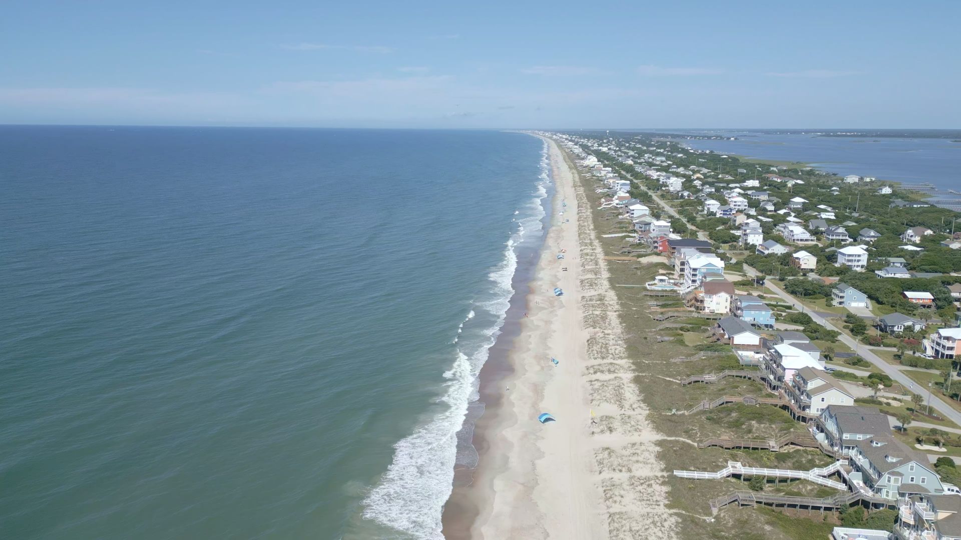 Aerial view of a long sandy beach beside blue water and a coastal neighborhood