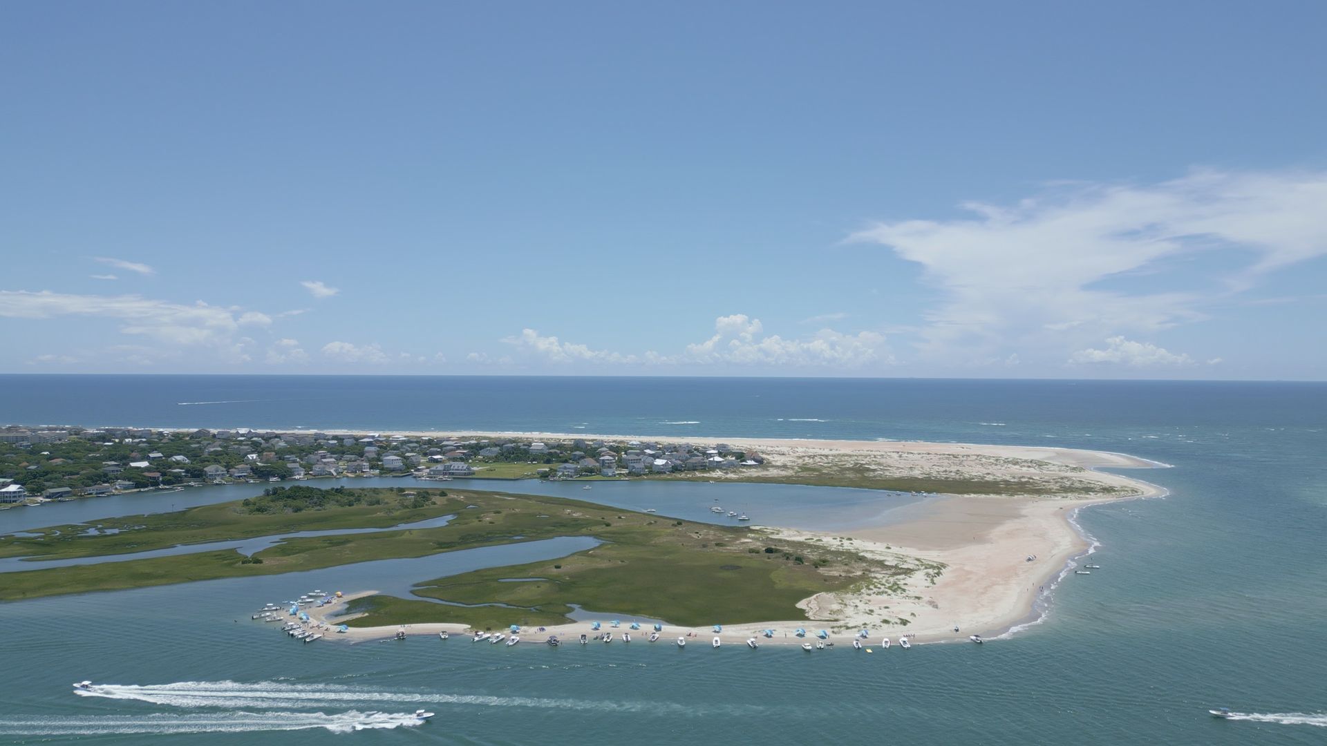 Aerial view of a sandy beach, blue ocean, and coastal marshland under a clear sky.