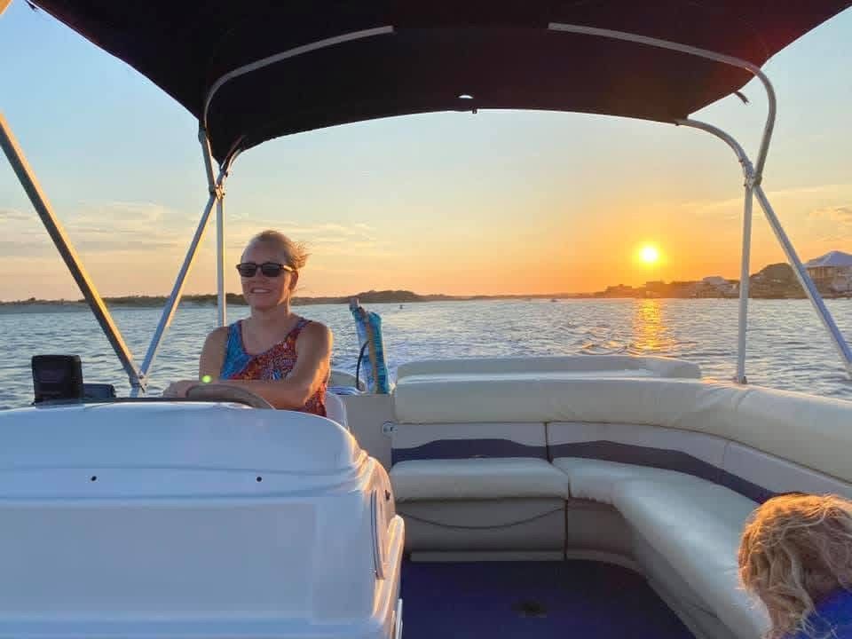 Person sitting on a boat at sunset, with calm water and a small dog in the foreground.