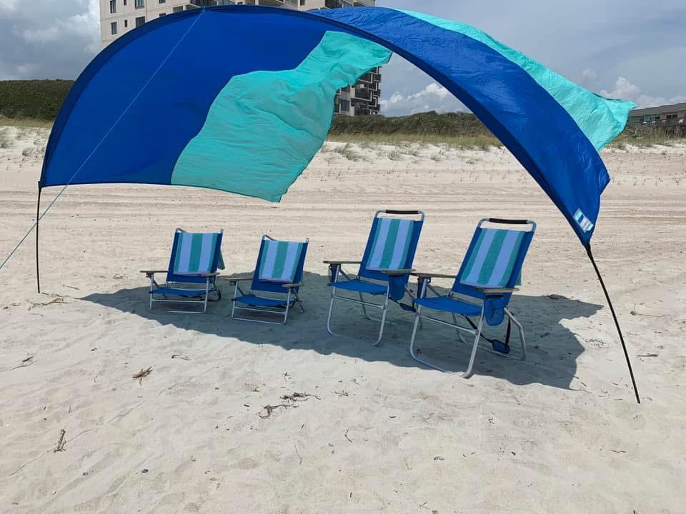 Four blue beach chairs under a blue sunshade canopy on a sandy beach