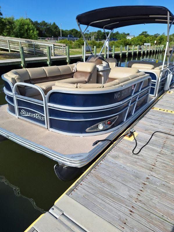 Pontoon boat with beige seats and a black canopy docked beside a wooden marina dock.