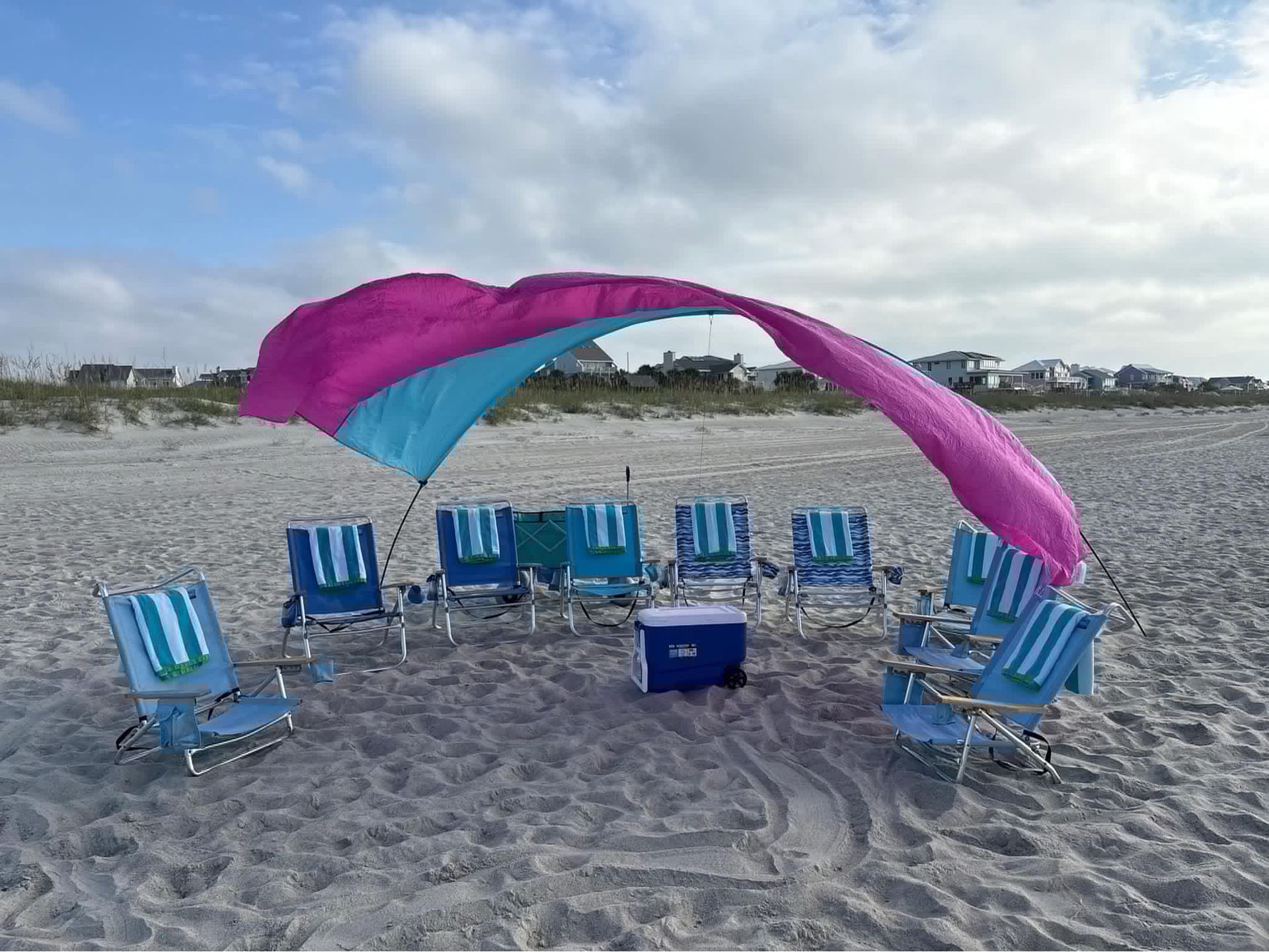 Beach setup with blue chairs in a circle under a pink-and-blue canopy on the sand