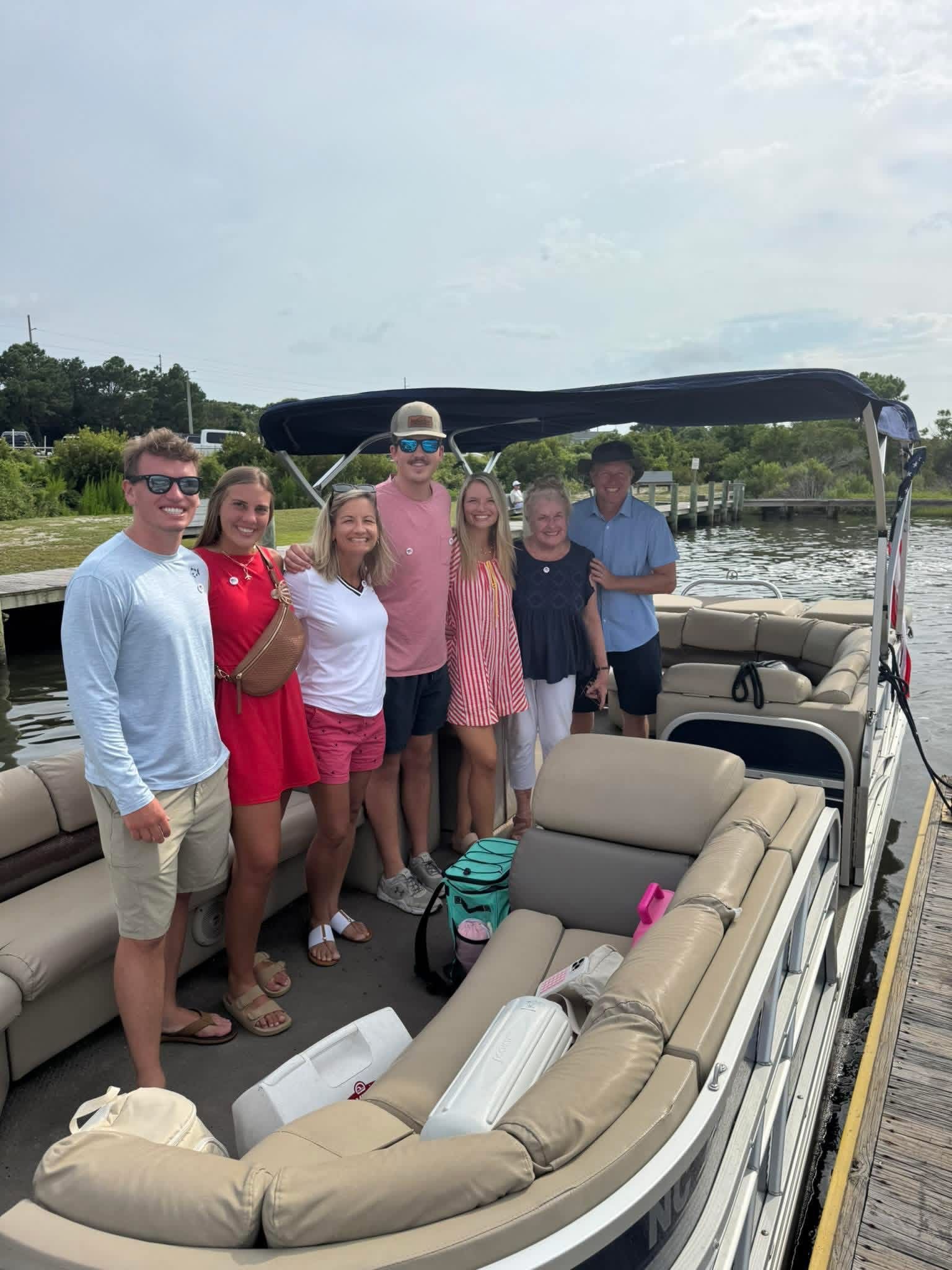 Group posing on a pontoon boat in a marina, with beige seats and water in the background.