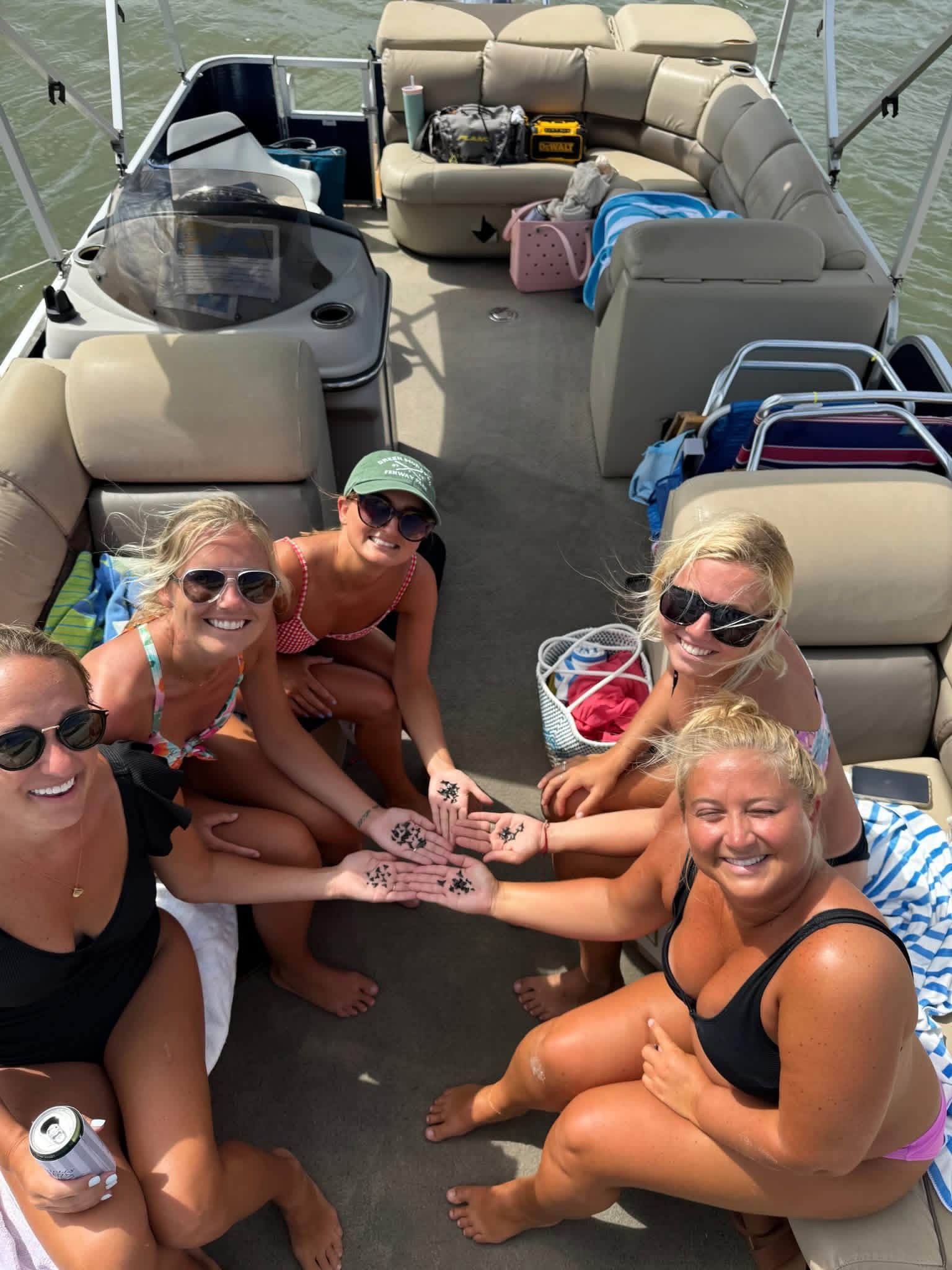 Six women sitting on a pontoon boat, smiling and holding their feet together in a circle.