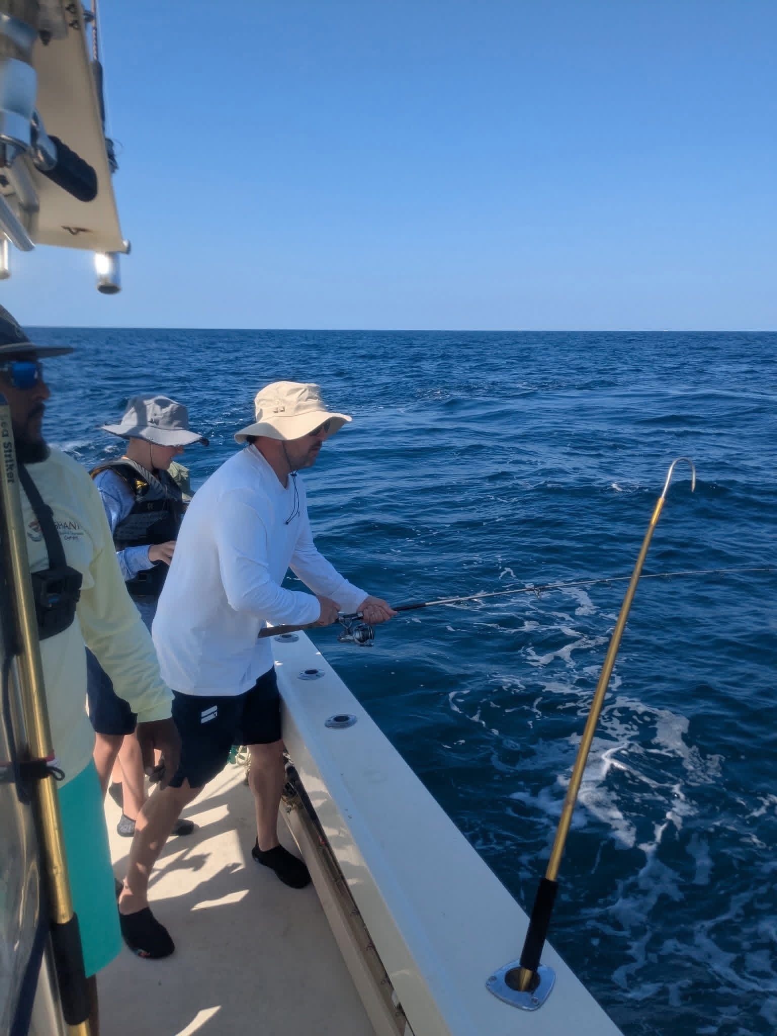 People fishing from a boat on a sunny ocean, with blue water and sky.