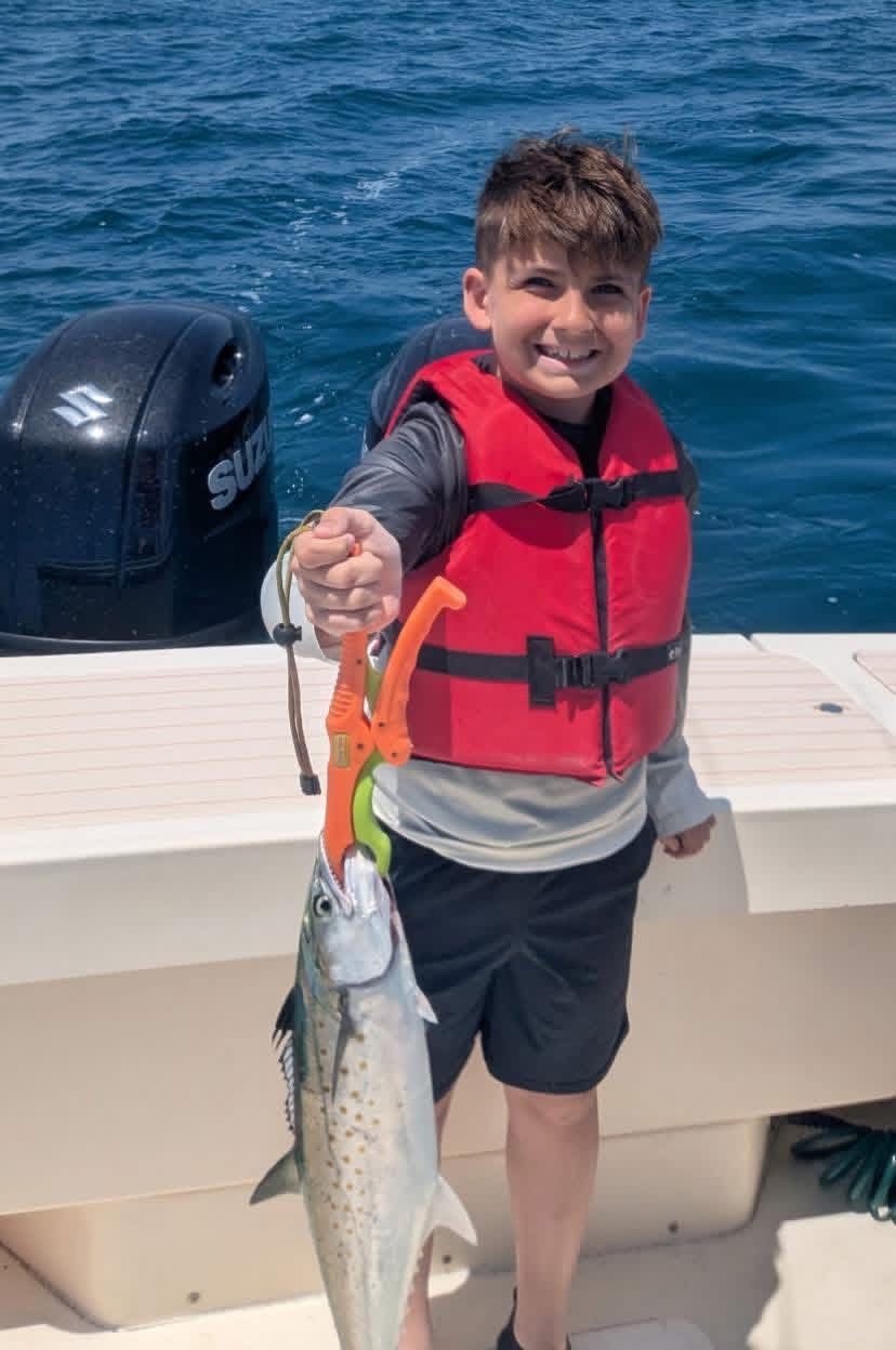 Boy on a boat holding up a large fish, wearing a red life jacket with ocean in the background
