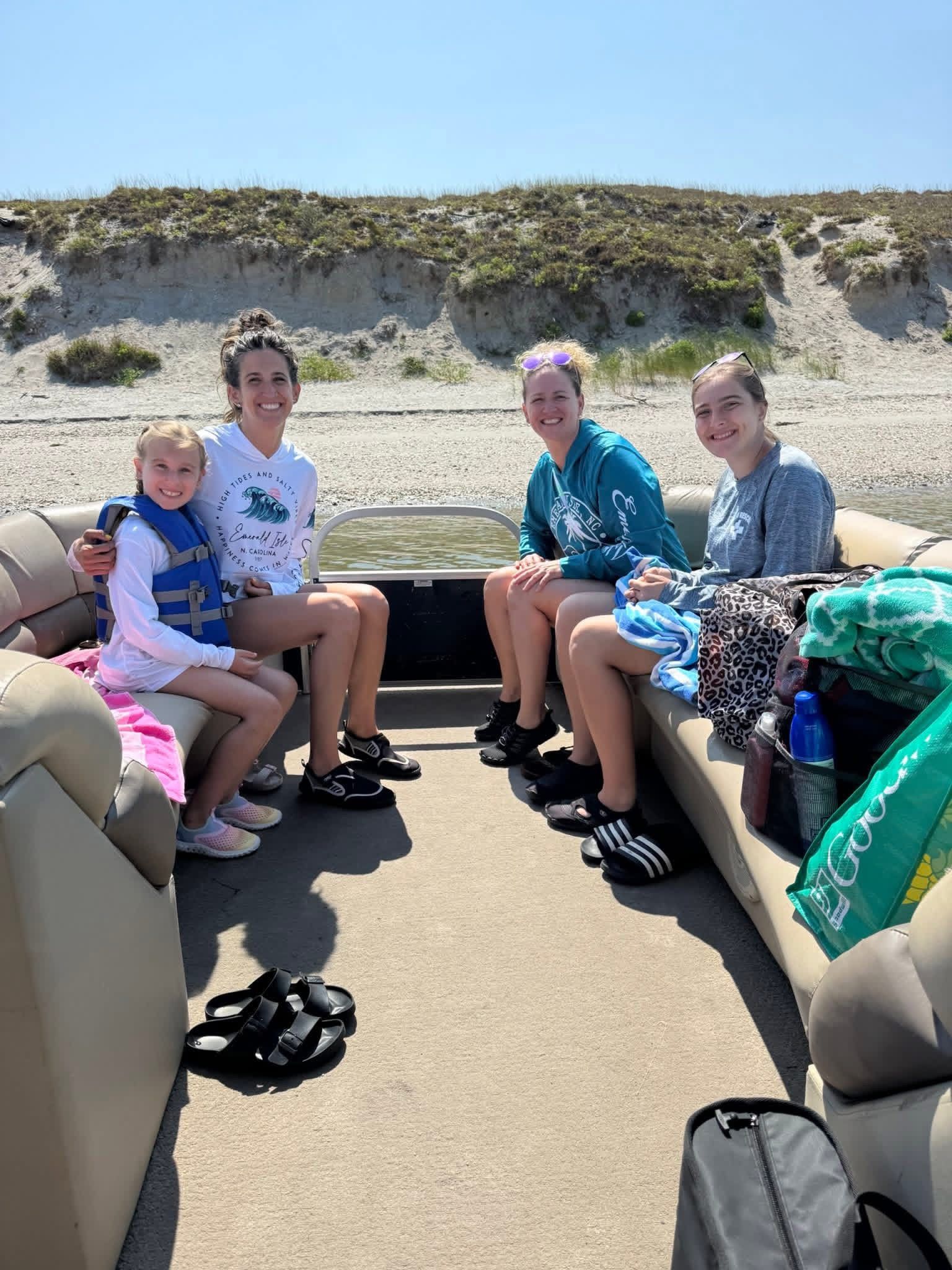 Five people sit on a beach vehicle bench seat, smiling in sunny sand dunes.