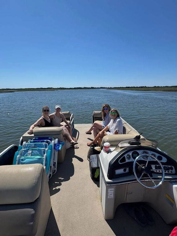 People lounging on two pontoon boats on a sunny lake, with a clear blue sky overhead.