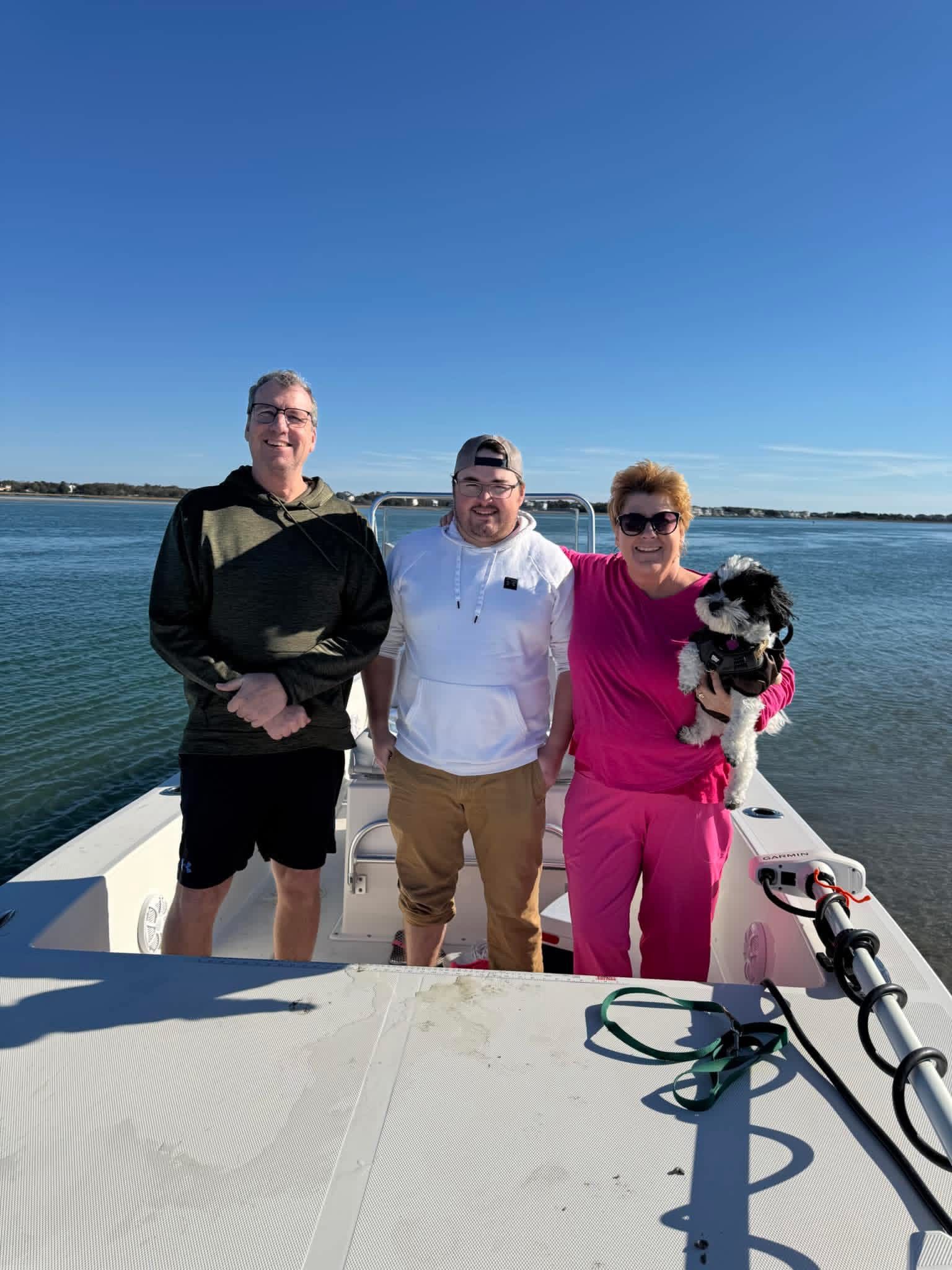 Three people and a dog on a boat deck with a blue sky and calm water in the background