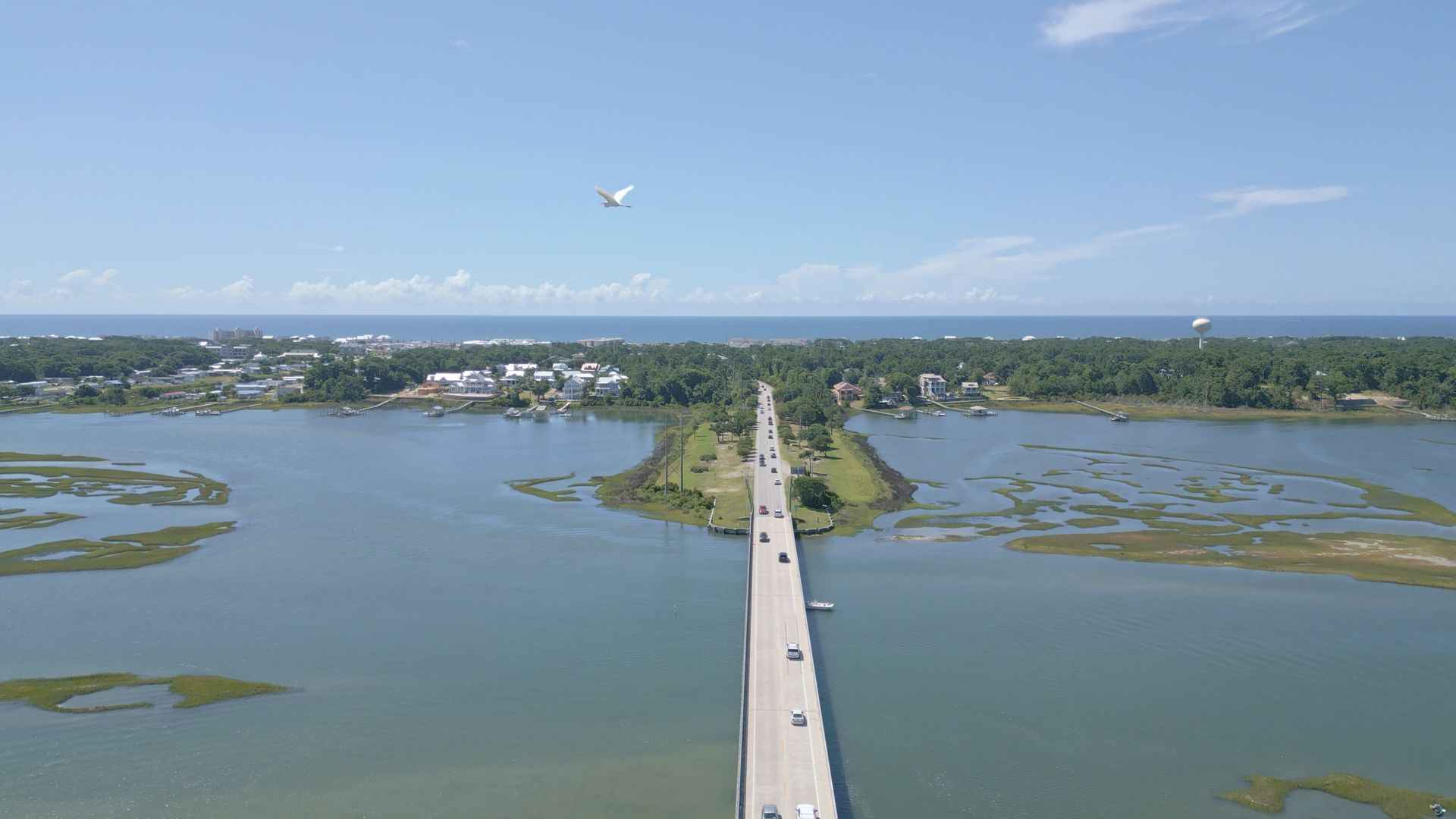 Aerial view of a long bridge over blue water leading to a coastal town under a clear sky