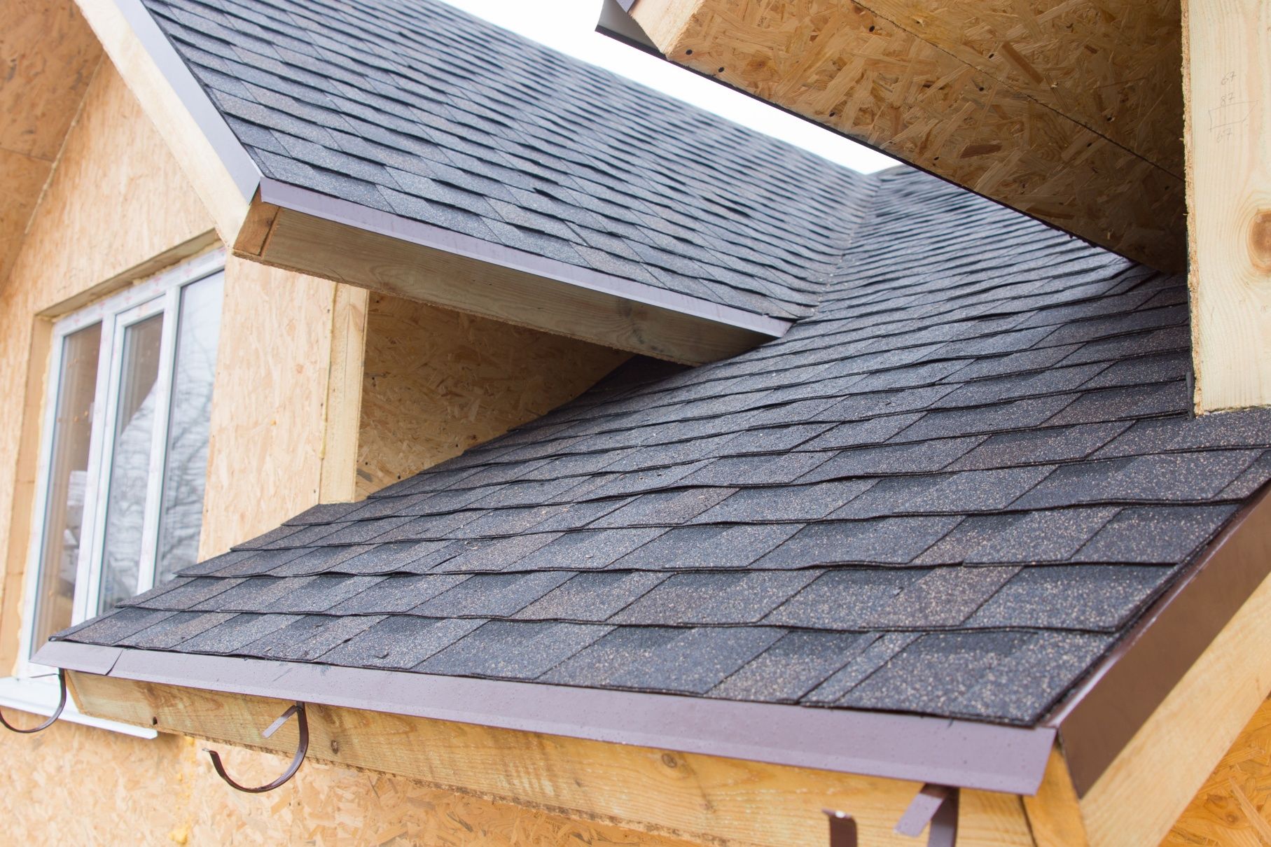 Partially constructed roof with dark shingles and brown trim.