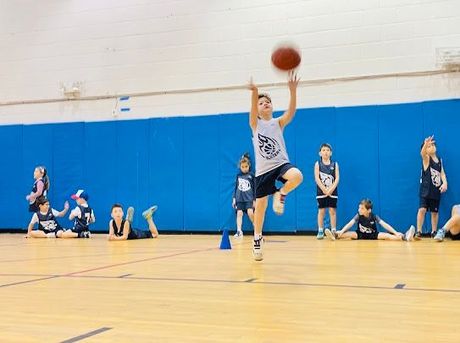 Basketball player leaping for a layup in a gym while teammates sit along the wall