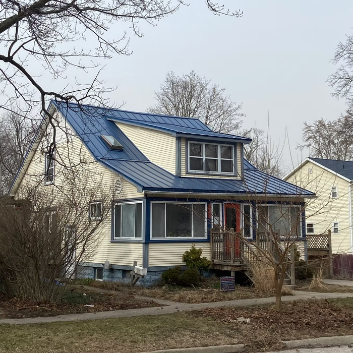 House with blue metal roof, white siding, and blue trim. Overcast day.