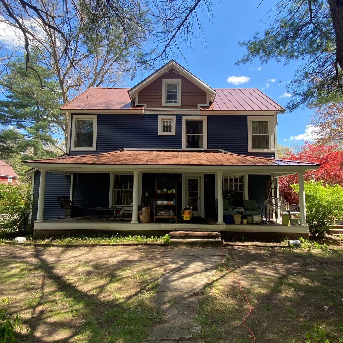 Blue two-story house with a wrap-around porch, brown roof, and several windows. Sunny day.