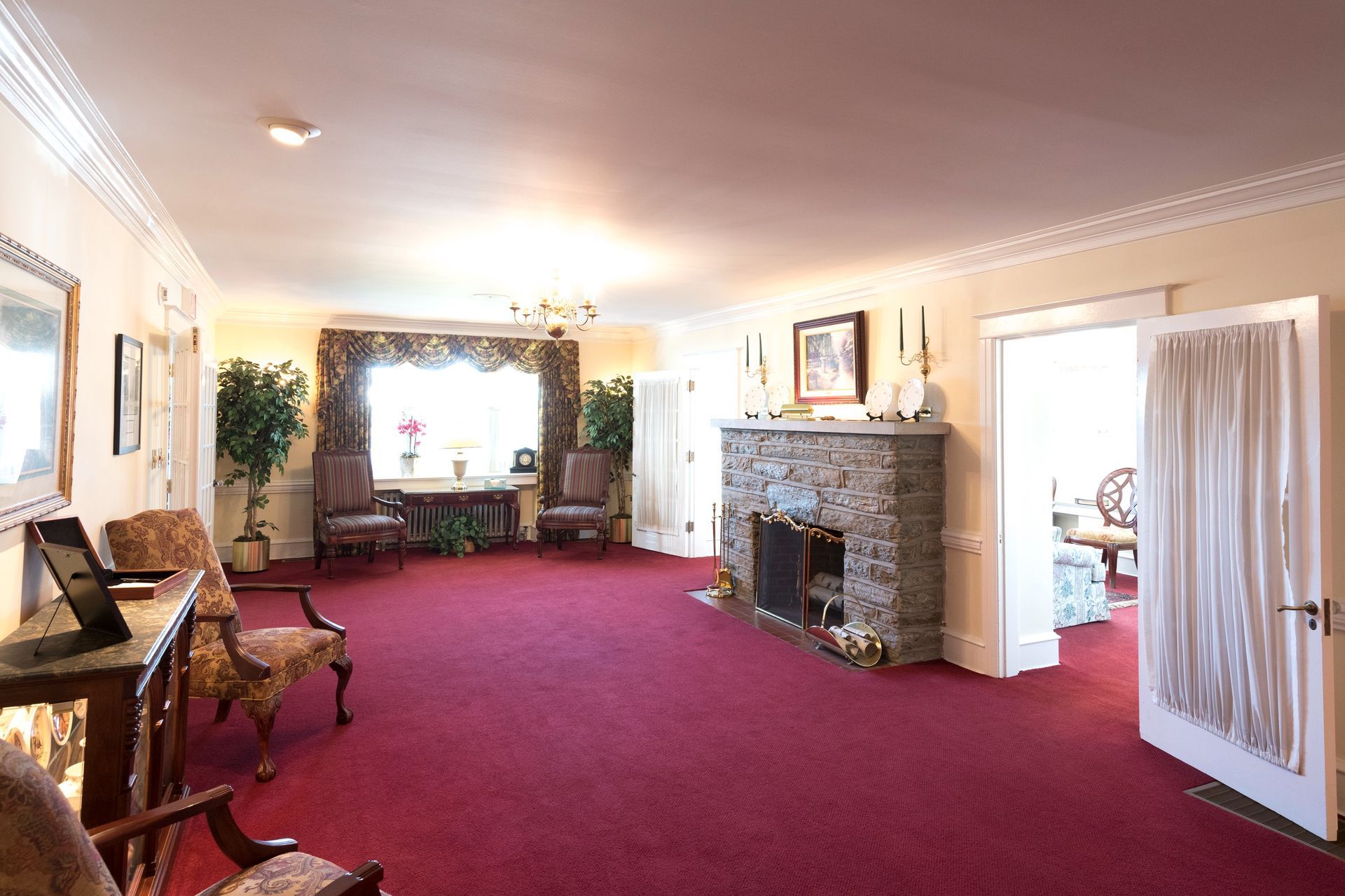 Elegant living room with red carpet, fireplace, piano, and large window seating area