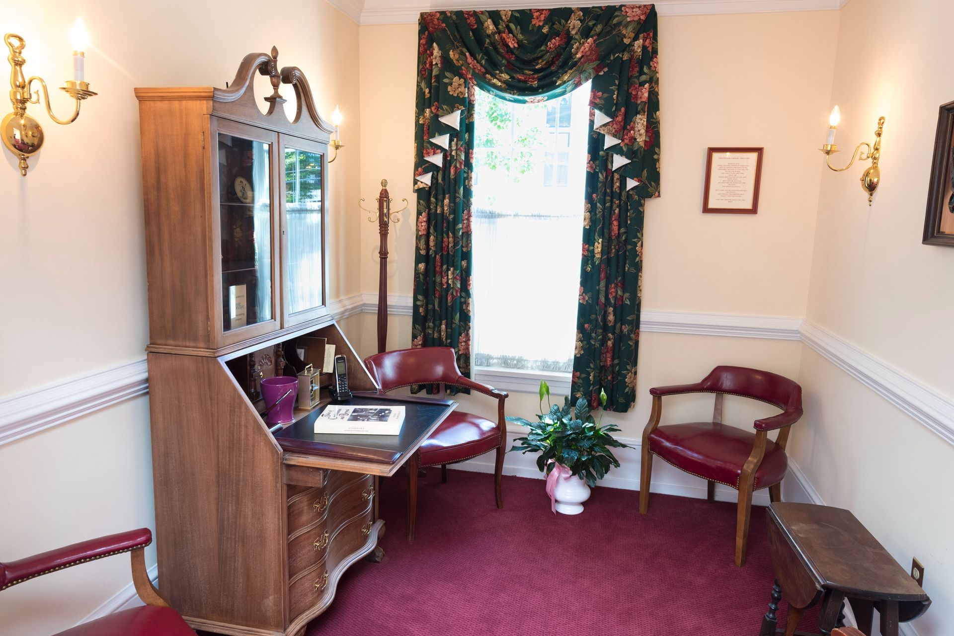 Elegant sitting room with burgundy carpet, wooden cabinet, chairs, and a large curtained window