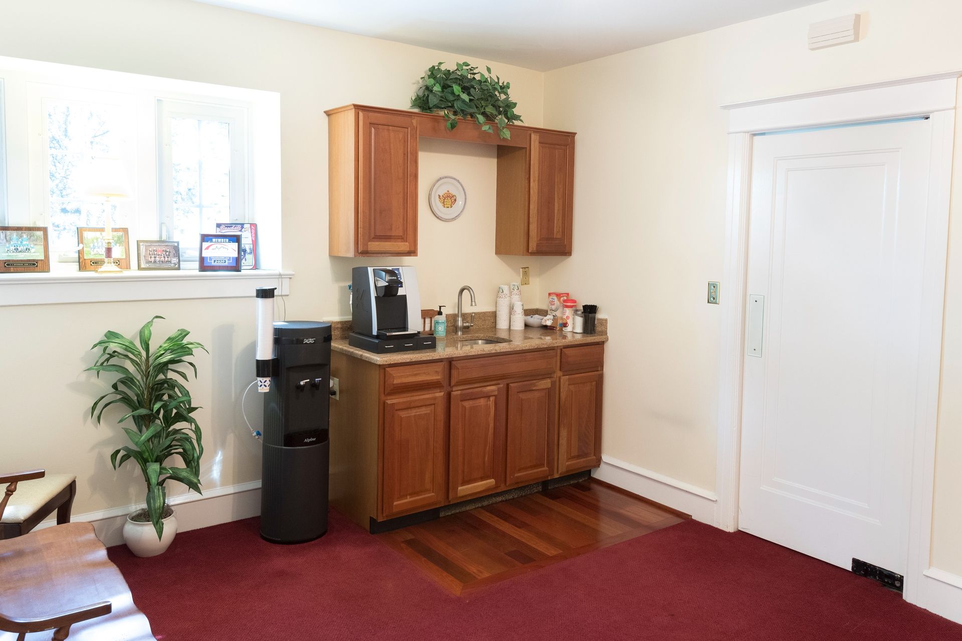 Living room nook with wooden cabinets, coffee maker, plant, red rug, and a closed white door